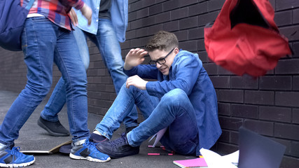 Students throwing things out of backpack on boy head, teenage bullying at school