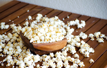 Salted popcorn on a wooden table. White popcorn flakes in a wooden bowl. Selective focus image.