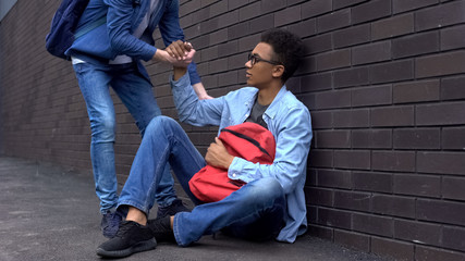 Teenage student giving helping hand to bullied afro-american boy, stop racism