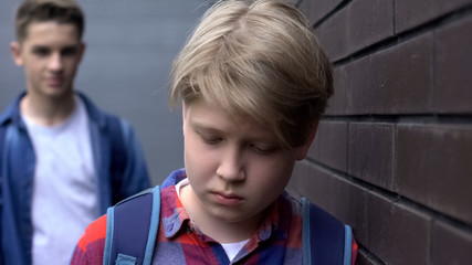 Bullied boy leaning against wall, scared of offender behind, intimidation