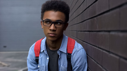 Depressed black boy victim of racial bullying standing near wall, loneliness