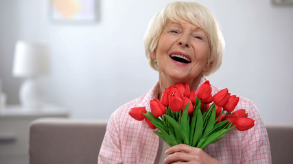 Extremely happy senior woman enjoying bunch of tulips, gift for anniversary