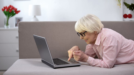 Smiling aged woman chatting on laptop with family, studying social networks