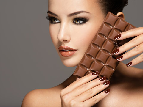 Beautiful woman with brown nails holds bar of chocolate
