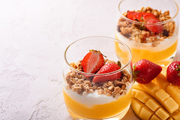 close-up of two glasses with fruit dessert of mango smoothie, ricotta cheese, granola and strawberry with beautifully sliced mango and copy space on pink background