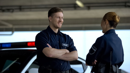 Happy male and female police officers talking near car, satisfied with good job