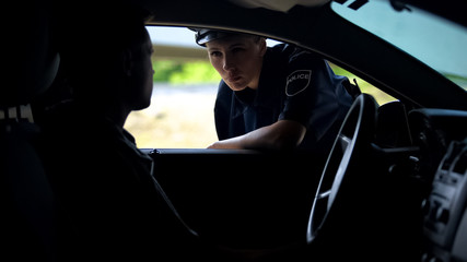 Police woman talking with driver in car, inspection on road, traffic offence