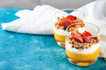 vegetarian dessert with mango and strawberry in glasses with white napkin on blue background