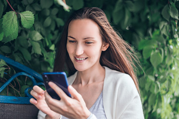 smiling girl sitting on bench looking into smartphone