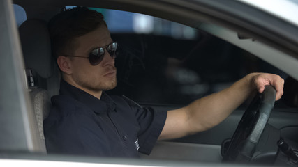 Confident policeman sitting in patrol car and wearing sunglasses, ready for work
