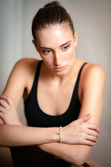 Portrait of a beautiful girl in black underwear looking aside while sitting over white background. Fashionable, commercial, advertising photoshoot. Vertical shot. Front view