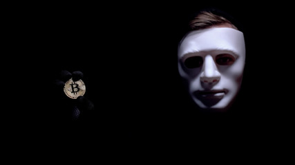 Man showing bitcoin, fearful anonymous mask on face, cyber attack, robbery