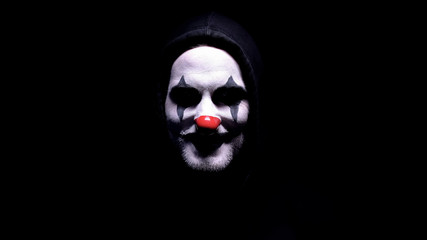 Maniac with spooky clown face angrily smiling into camera, psycho threatening
