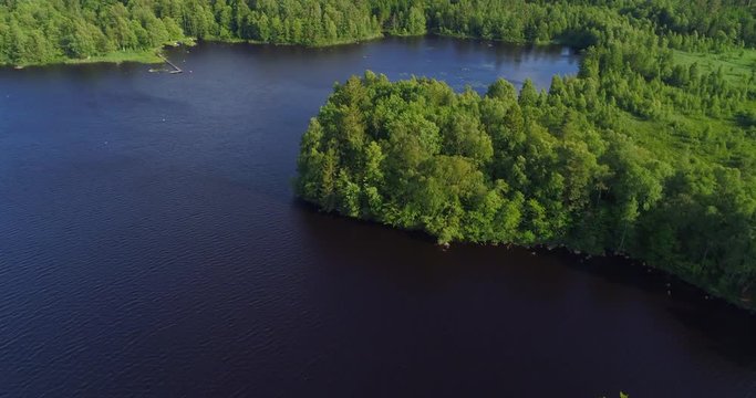 Aerial: Drone footage of lake by trees on landscape against blue - Smaland, Sweden