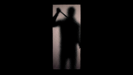 Fearful silhouette of man with knife standing near glass door maniac breaking in