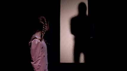 Girl looking at silhouette of criminal entering room, kidnapping concept, horror