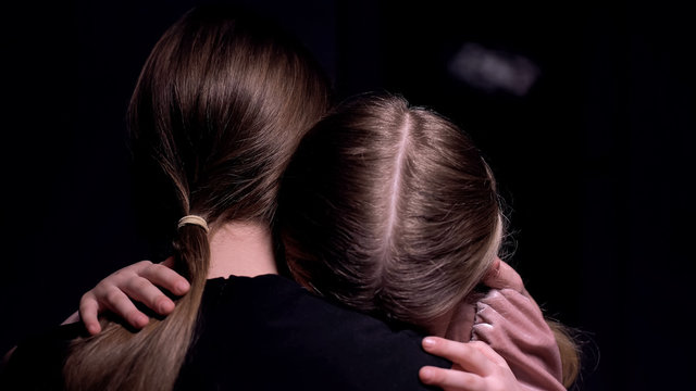 Mother hugging frightened little girl in dark room, victims of mafia, kidnapping