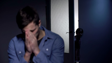 Depressed father crying in room, little daughter opening door, pain of loss