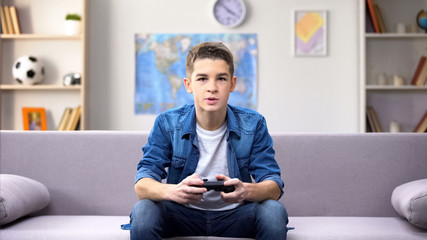 Focused teenage boy playing video game at home, gadget addiction in awkward age