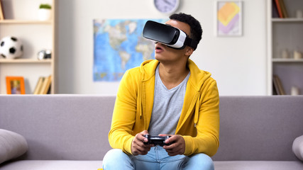 African-American teen boy with joystick playing video game in VR headset, future © motortion