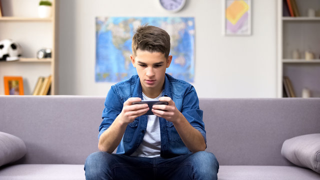 Gadget addicted Caucasian teenager playing game on smartphone, wasting time