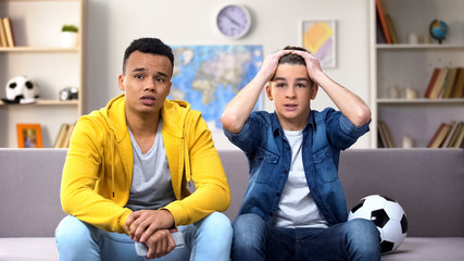 Anxious teenagers watching football match on TV unhappy with team losing, sport