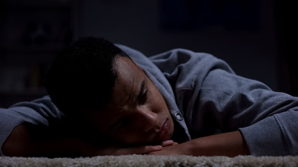 Unhappy afro-american teenager lying on floor, suffering racial discrimination