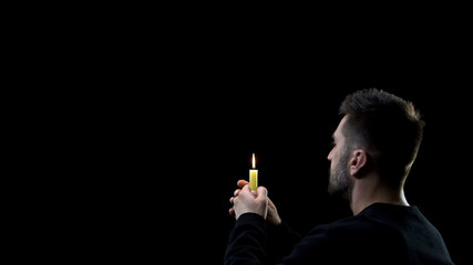 Fototapeta premium Praying man holding burning candle on dark background, spiritual ritual, faith