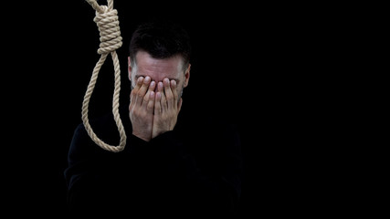 Disappointed crying man near loop on dark background, feeling lonely, loss