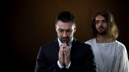 Praying businessman joining hands, messiah standing behind, spiritual support