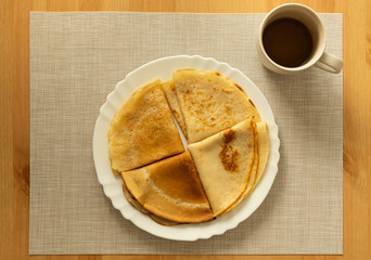 Four pancakes on white plate and coffee on table.