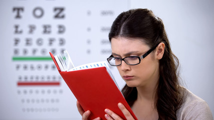 Woman in glasses suffering myopia reading book, need in correct lens diopter