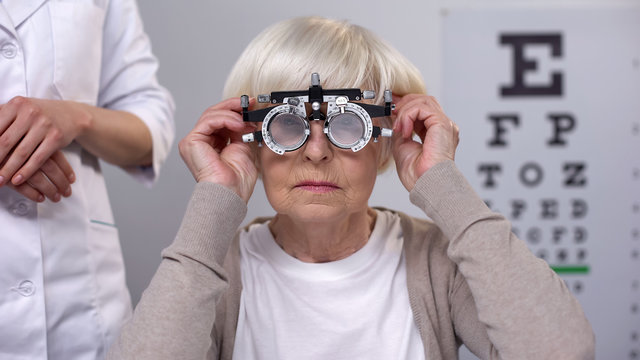 Doctor putting phoropter on elderly woman eyes, choosing proper lens diopter