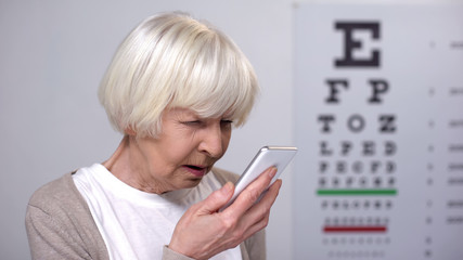 Senior woman with poor vision using smartphone, rejecting to wear eyeglasses