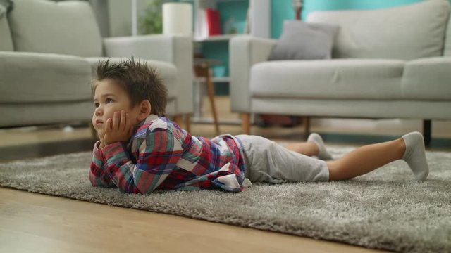 Little boy watches cartoons on TV lying on the floor in living room