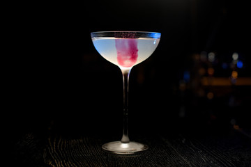 Glass with a pink ice cube and light blue cocktail standing in tha bar