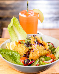 A plate of Crispy Calamari Salad with lettuce, radish, lemon, tomatoes, asparagus  and avocado.