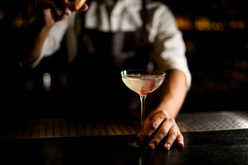 Professional bartender serving a cocktail in the glass decorated with pink ice cube