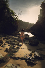 A girl in a swimsuit is walking along the beach. Ocean coast. Bali. Bingin Beach. Asia. Journey. Rocks on the beach.