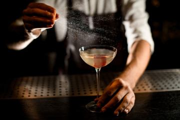 Professional bartender serving a cocktail in the glass adding a lemon juice
