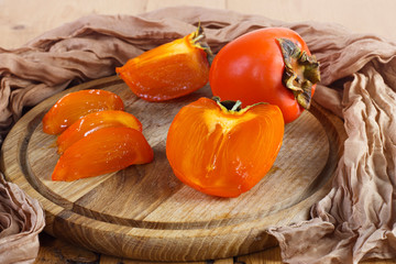 Autumn fruits. Persimmons on a wooden board on a wooden background on a napkin.