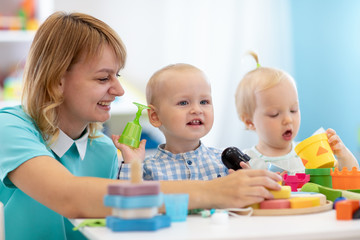 Obraz na płótnie Canvas Kindergarten babies together with teacher playing educational toys at sunny day in nursery