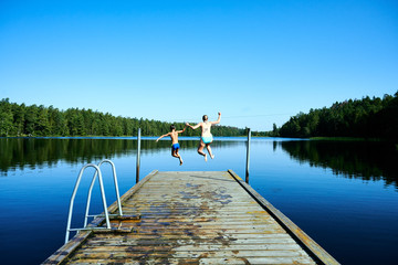 Frau und Kind springen in Bade See vom Steg aus im Familienurlaub