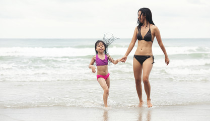Happy little asia girl with her mother running on the beach.