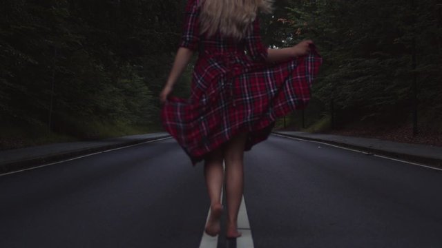 Beautiful millennial woman walking down the middle of an abandoned road surrounded by nature.