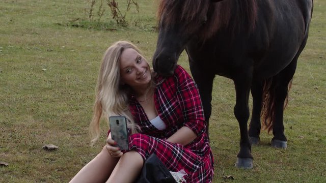 Blonde girl sitting and taking pictures with pony. Static