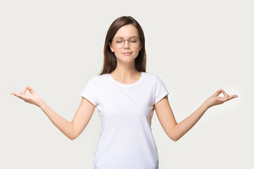 Focused young woman in glasses meditating in studio