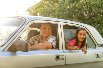 Senior man driving car with his granddaughter sitting behind with dog, looking through window