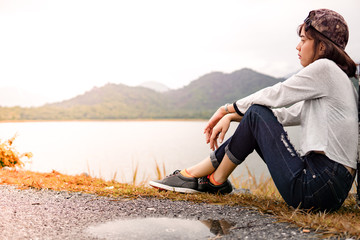 asian Woman wear hat leaning on The road in the large lake and mountains in the background , copy space