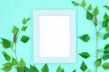 Top view summer flat lay with photo frame and green leaves arrangement on a mint background. Copy space for text